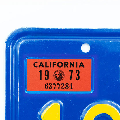 California license plate 1973 year sticker applied to upper corner of blue California plate — YOM Series